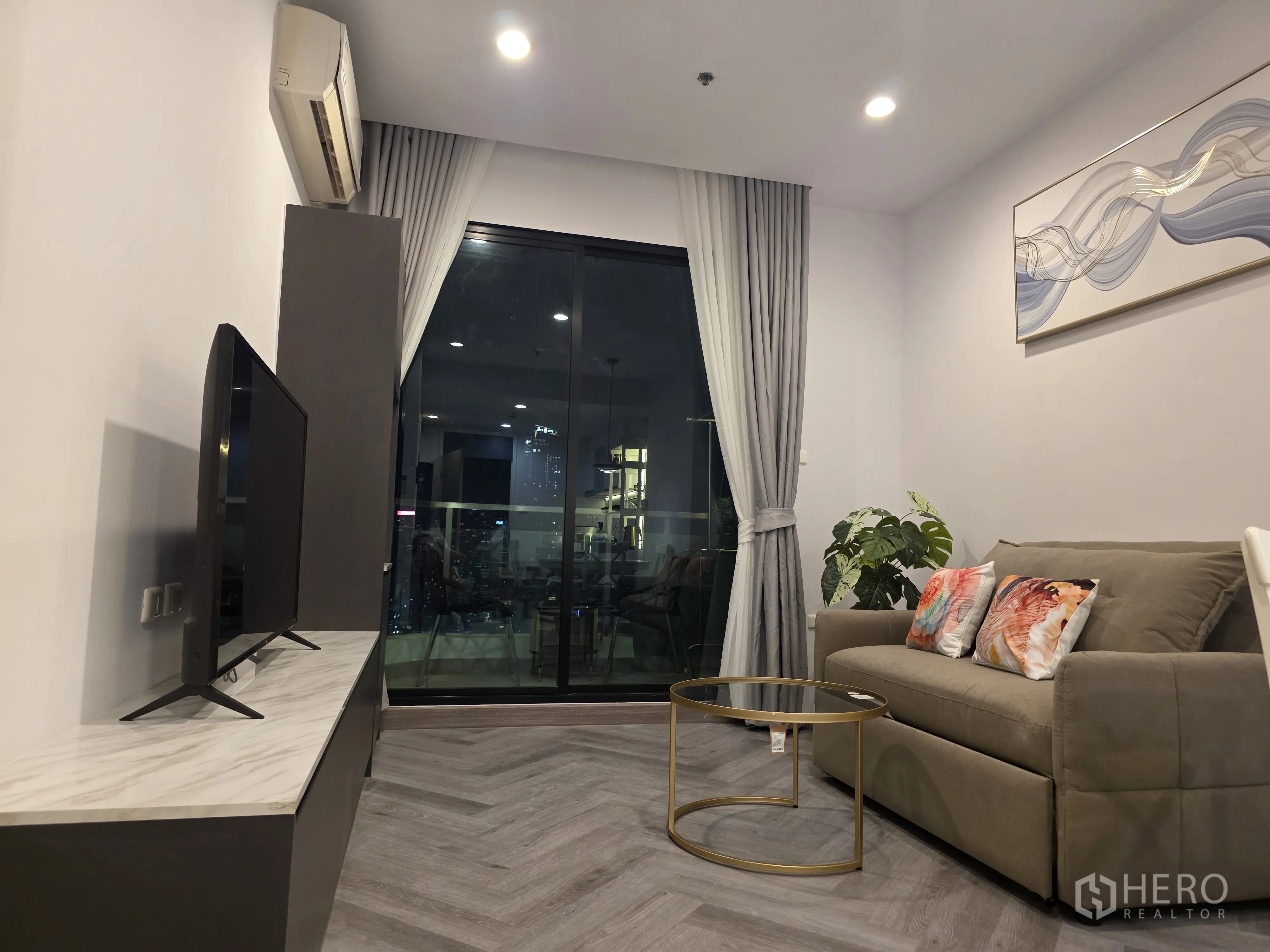 Condominium for rent in Bang Kapi, Bangkok - Living room with sofa, TV console, and large sliding glass door.