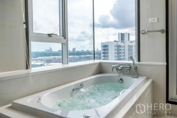 Apartment for rent in Khlong Toei, Bangkok - Corner bathtub with running water and large windows framing Bangkok skyline views.