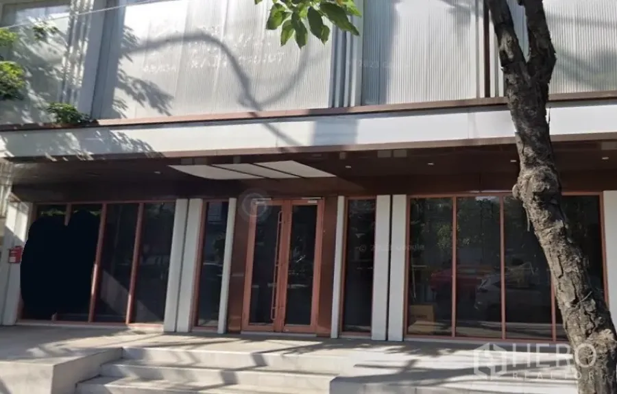 Shophouse for rent in Phra Khanong, Bangkok - Modern shophouse facade with floor‑to‑ceiling glass, shaded entrance and steps in Phra Khanong.