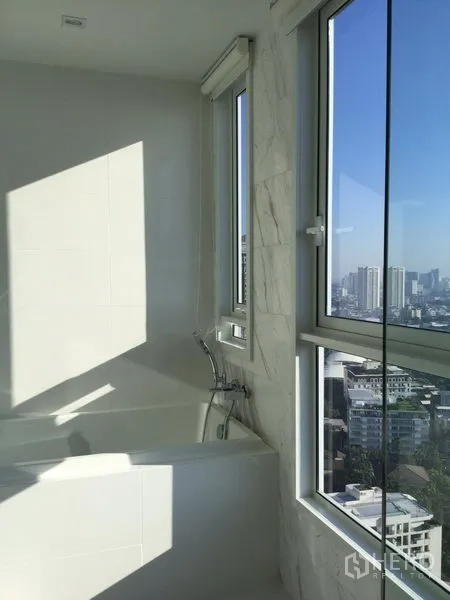 Condominium for rent or sale in Watthana, Bangkok - Bathroom with a bathtub beside corner windows overlooking the Bangkok skyline.