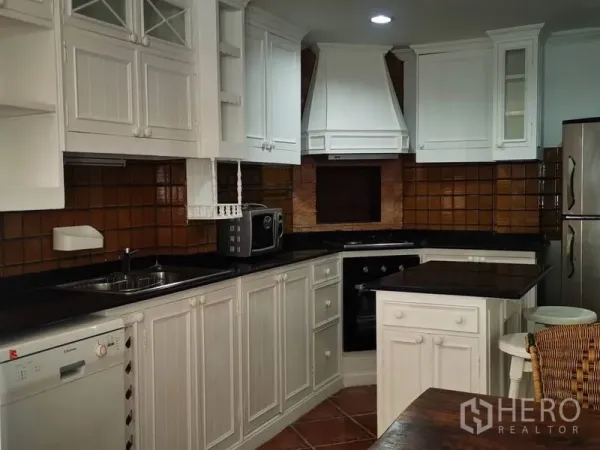 Detached House for rent in Mueang Samut Prakan, Samut Prakan - U-shaped kitchen featuring white cabinets, oven, cooktop, stainless refrigerator and stone countertops.