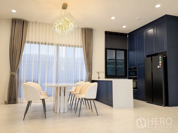 Detached House for rent in Bang Khen, Bangkok - Dining area and modern kitchen with navy cabinetry, island counter, chandelier and large windows.