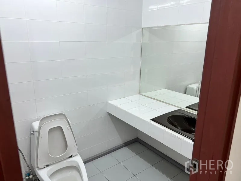 Office Space for rent in Pathum Wan, Bangkok - Clean office restroom with white tiled walls, toilet and a long vanity with large mirror.