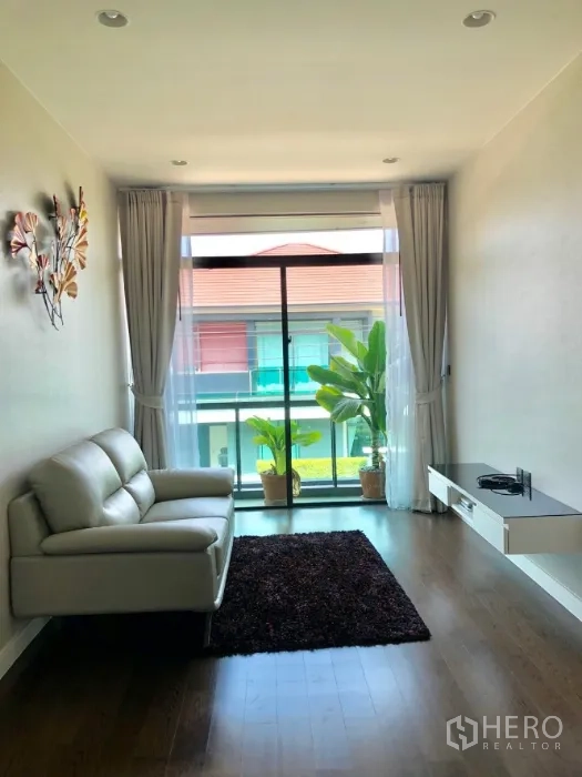 Detached House for rent in Bang Kapi, Bangkok - Upstairs lounge with white loveseat, sliding balcony doors, potted plants and a floating TV shelf.