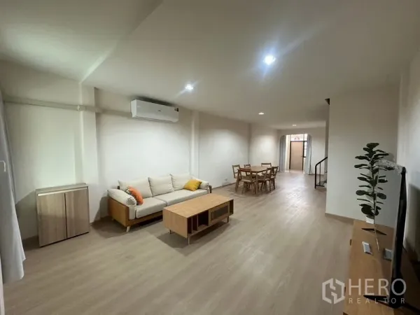 Townhouse for rent or sale in Phra Khanong, Bangkok - Open-plan living and dining area with wood floors, sofa set and recessed lights.
