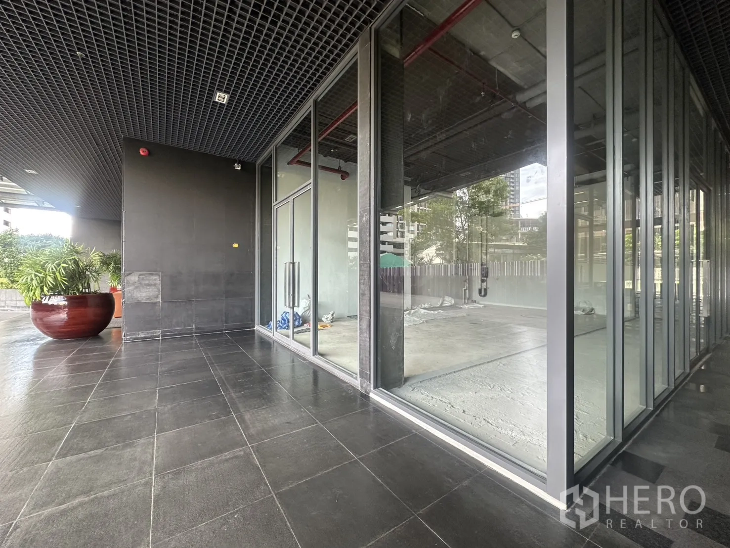 零售空间 for rent in Khlong Toei, Bangkok - 带顶室外走道与转角玻璃店面，配有绿植与铺砖平台。