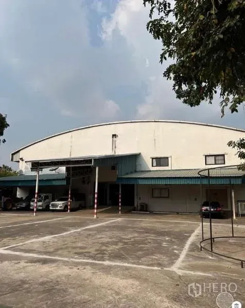 Warehouse for sale in Bang Bua Thong, Nonthaburi - Front exterior of a large arched‑roof warehouse with covered loading bays and wide parking yard in Bang Bua Thong.