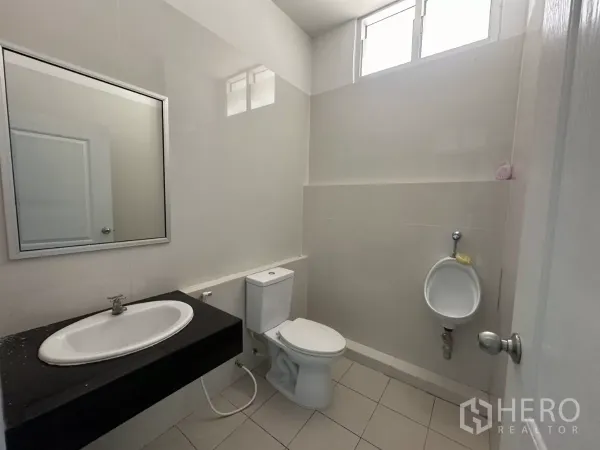 Factory for rent in Bang Phli, Samut Prakan - Clean restroom with sink, toilet and wall urinal, tiled walls and high window.