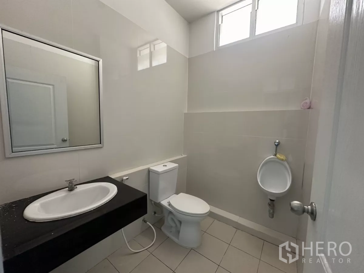 Factory for rent in Bang Phli, Samut Prakan - Clean restroom with sink, toilet and wall urinal, tiled walls and high window.