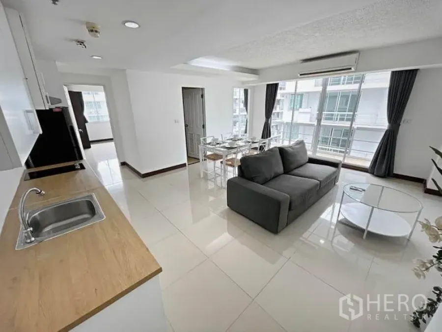 Condominium for rent in Khlong Toei, Bangkok - Bright open-plan living and dining area with grey sofa, six-seat table, and large windows.