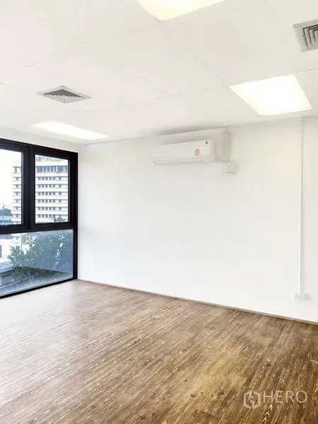 Office Space for rent - Corner of a white office room with split-type air conditioner, large window, and wood flooring.
