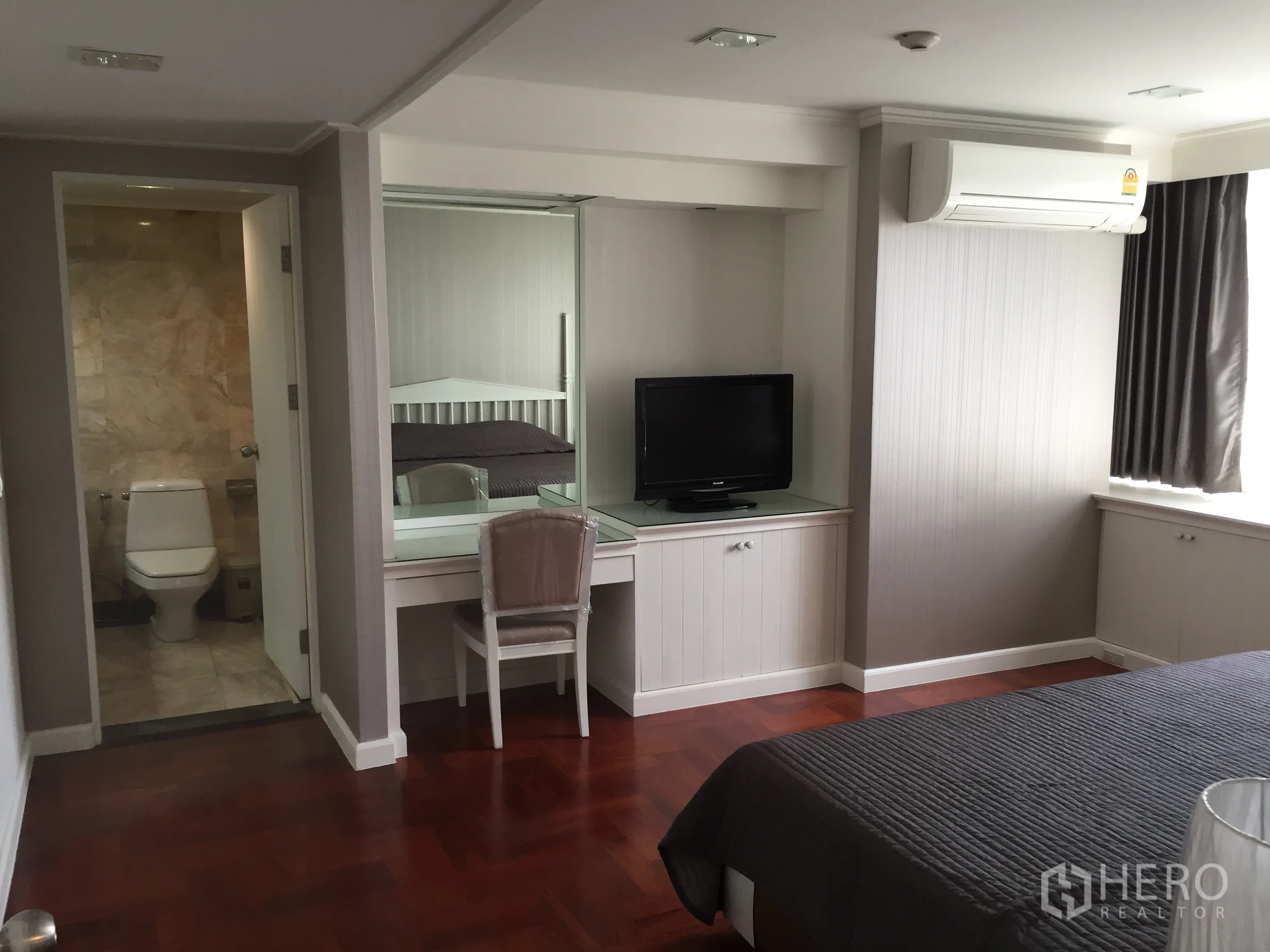 Condominium for rent in Khlong Toei, Bangkok - Master bedroom with ensuite bathroom, air conditioning, TV console, and large curtained window.