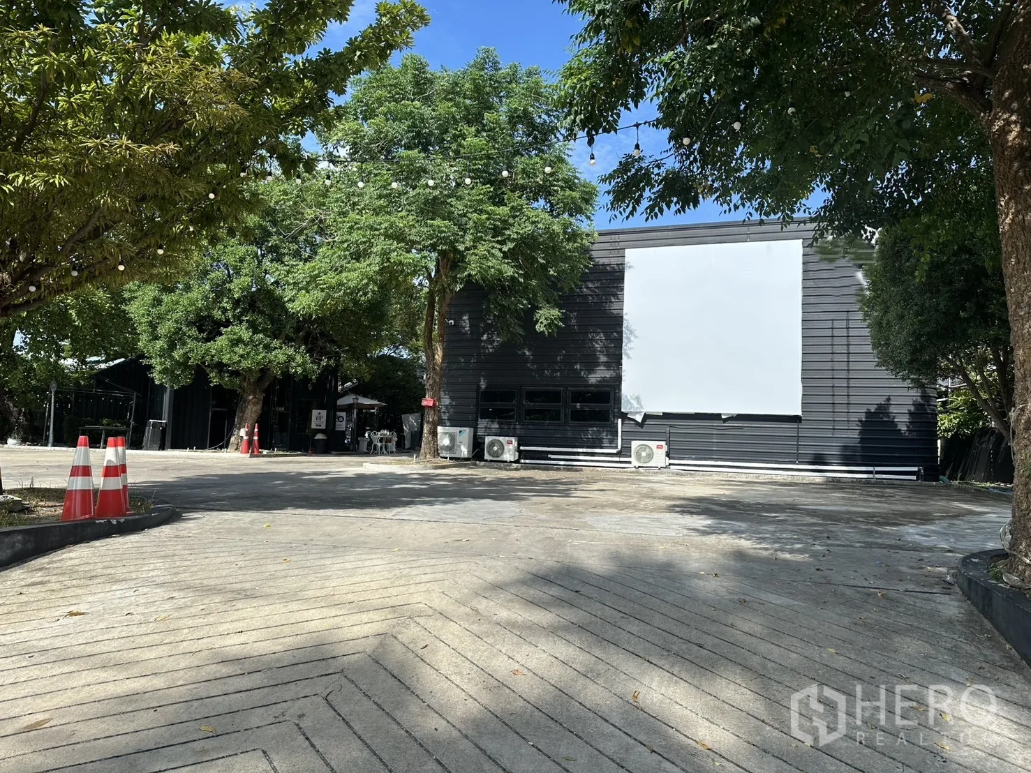 Warehouse for rent in Phra Khanong, Bangkok - Warehouse exterior with wide concrete forecourt, trees, and metal-clad building.