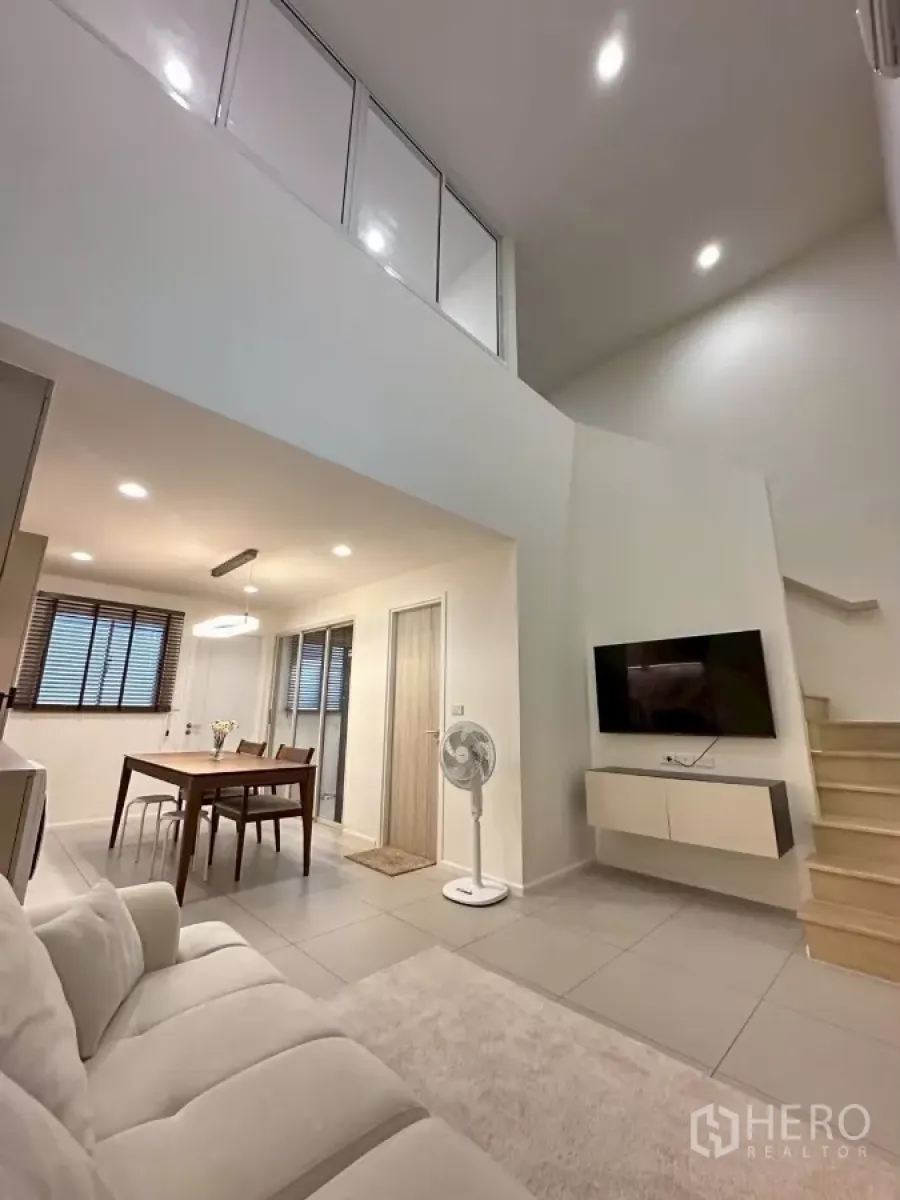 Townhouse for rent in Saphan Sung, Bangkok - Double-height living room with mezzanine glass railing, wall-mounted TV and stairs in a modern townhouse.