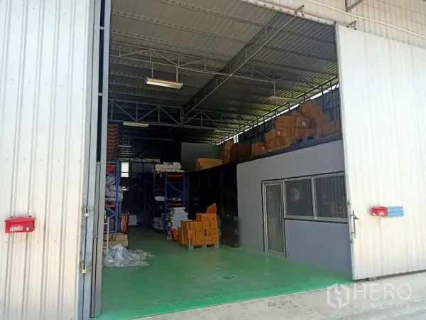 Warehouse for rent in Bang Kapi, Bangkok - Open sliding doors show a high-clearance warehouse interior with steel trusses, green epoxy flooring, and storage racks.