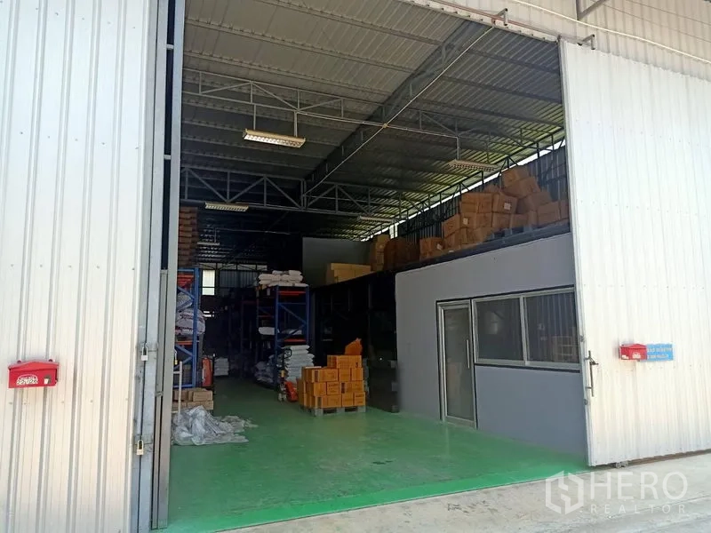 Warehouse for rent in Bang Kapi, Bangkok - Open sliding doors show a high-clearance warehouse interior with steel trusses, green epoxy flooring, and storage racks.
