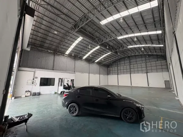 Warehouse for rent in Bang Phli, Samut Prakan - Spacious warehouse interior with high arched steel roof, skylight panels, and a small office corner.