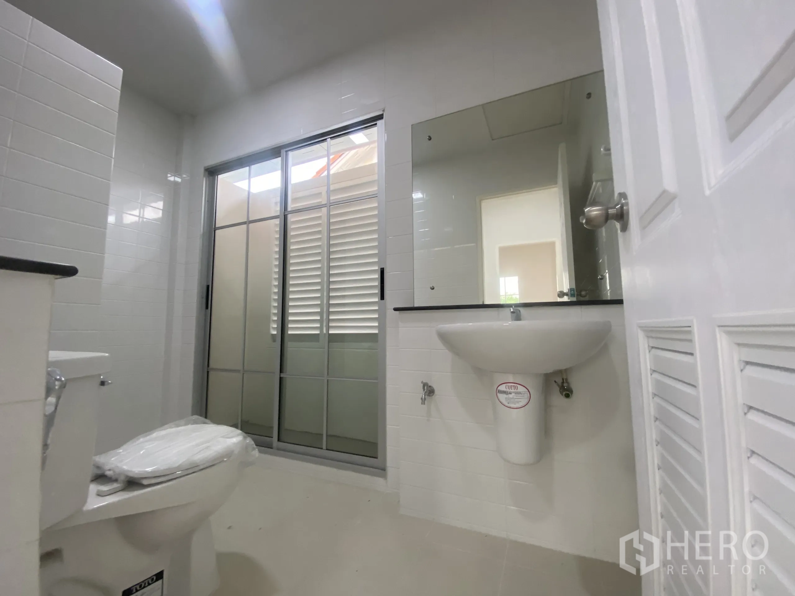 Detached House for sale in Nonthaburi - Upstairs bathroom with large mirror, toilet and a frosted sliding door.