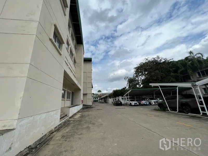 货栈 出租在Bang Kapi, Bangkok - 园区内宽阔道路，仓库旁设有带顶停车位与成荫树木。