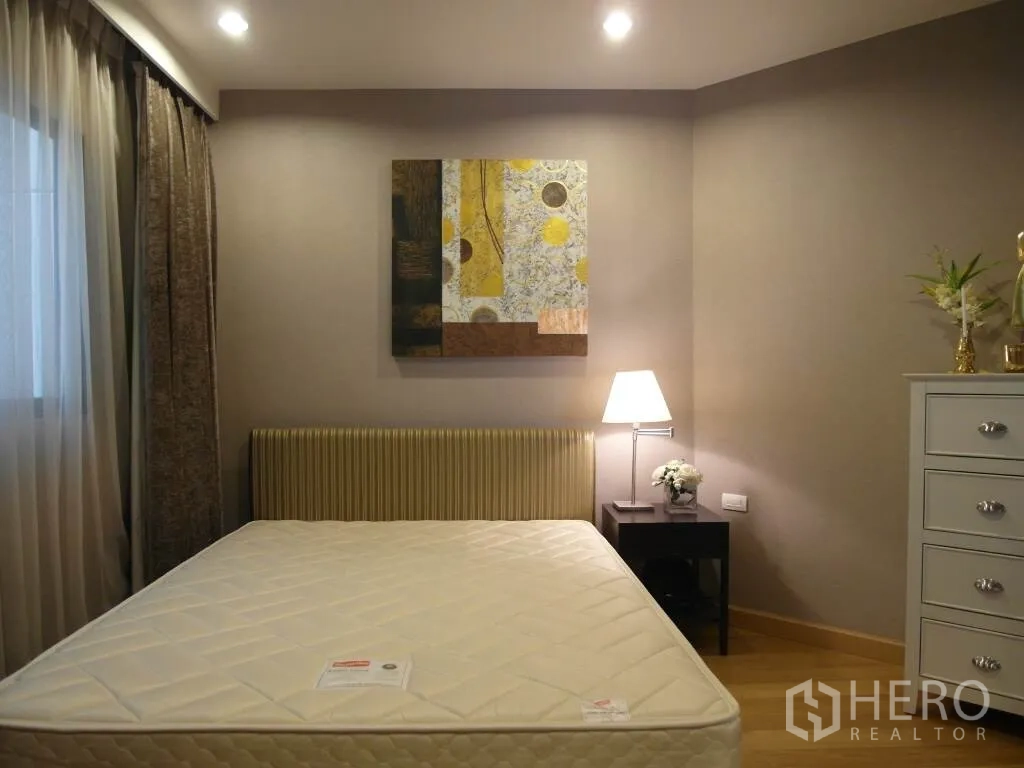 Condominium for rent or sale in Sathon, Bangkok - Cozy second bedroom with bed and mattress, bedside lamp, artwork and curtains.