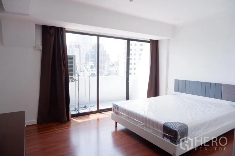 Condominium for rent in Khlong Toei, Bangkok - Master bedroom opening to a glass sliding-door balcony with city view and large bed.