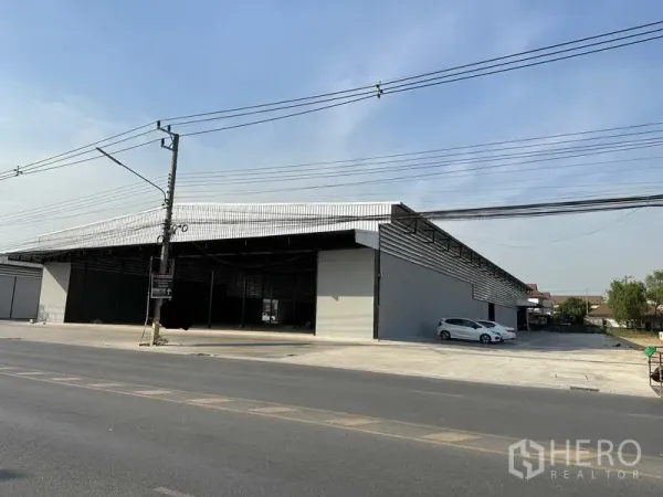 Warehouse for rent in Lam Luk Ka, Pathum Thani - Street-facing view of a large metal-clad warehouse with wide open bay and broad concrete forecourt.
