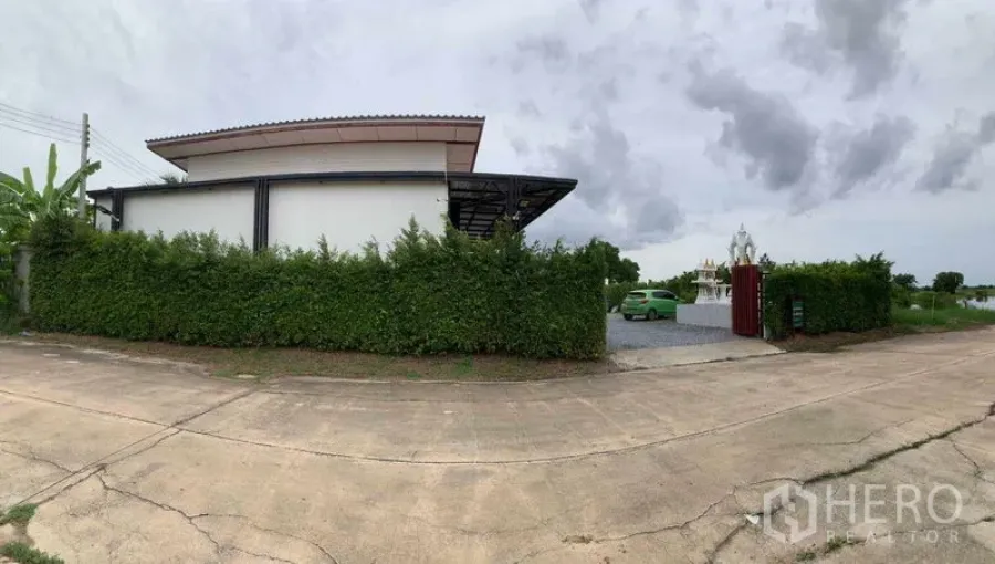 Factory for sale in Bang Pa-in, Phra Nakhon Si Ayutthaya - Panoramic street view of the gated factory screened by a tall hedge with a wide driveway.