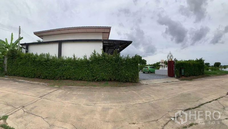 Factory for sale in Bang Pa-in, Phra Nakhon Si Ayutthaya - Panoramic street view of the gated factory screened by a tall hedge with a wide driveway.