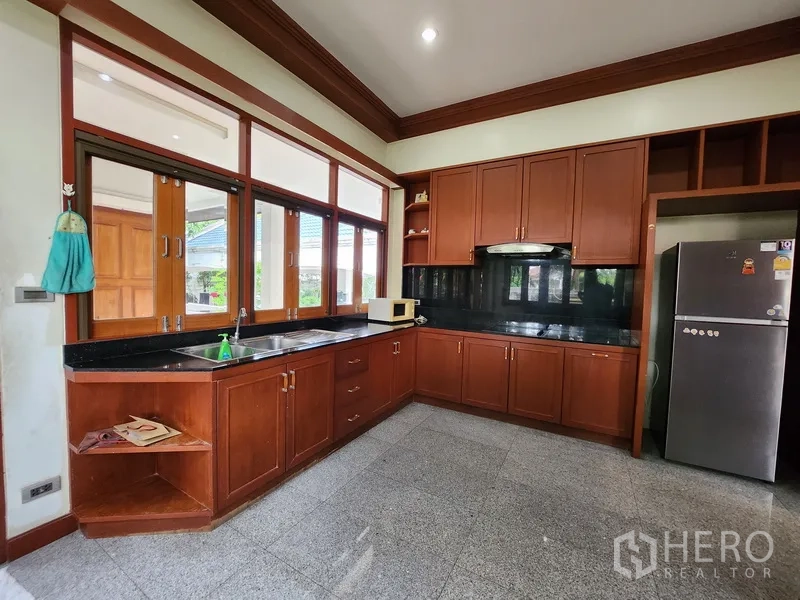 Detached House for rent in Prawet, Bangkok - Family kitchen with wooden cabinets, black stone countertops, range hood and large windows.