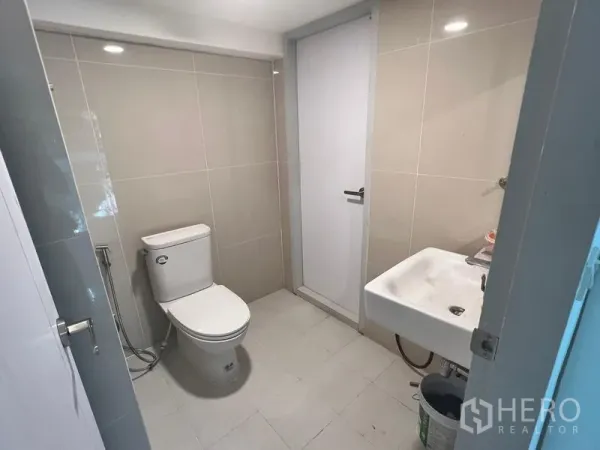 Shophouse for rent in Khlong Toei, Bangkok - Modern tiled restroom featuring a toilet, handheld bidet and wall-mounted sink.