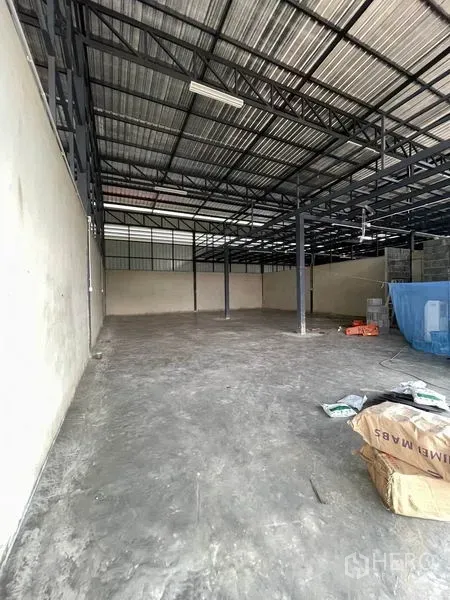 Warehouse for rent in Pathum Thani - Long interior view of empty storage space under a metal roof with tools and materials on the floor.