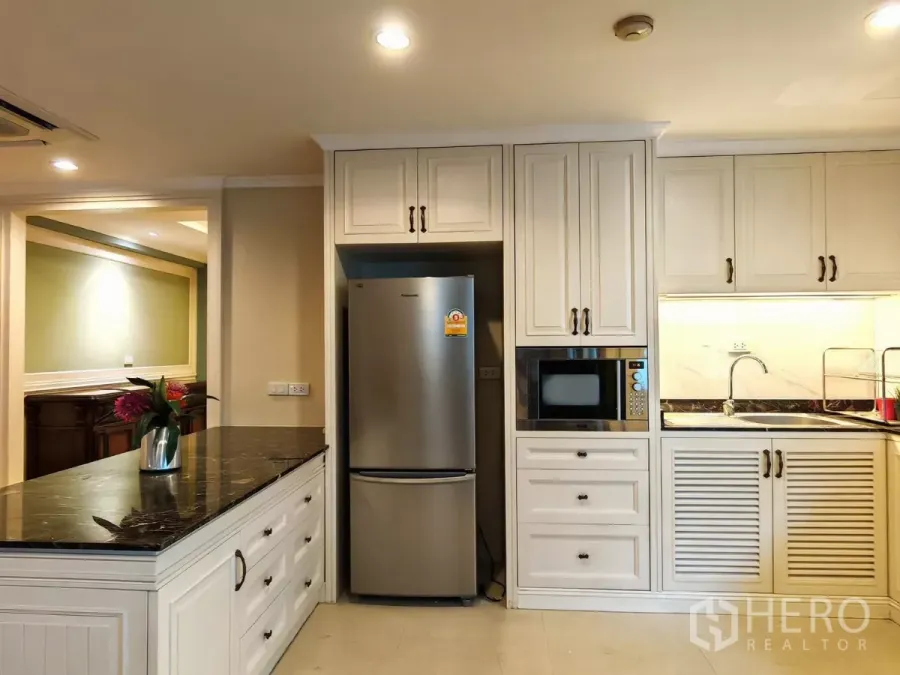 Condominium for rent in Pathum Wan, Bangkok - Modern kitchen with stainless refrigerator, microwave and black stone countertops.