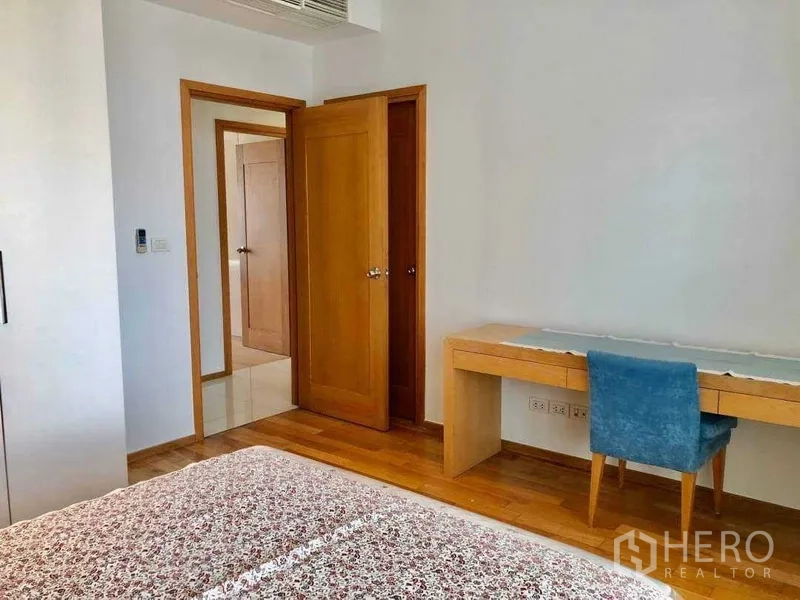 Condominium for sale in Khlong Toei, Bangkok - Third bedroom with a long study desk and blue chair on wood flooring.