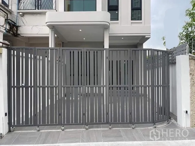 联排别墅 出售在Watthana, Bangkok - 前院可停车，近景金属折叠门与有顶车棚