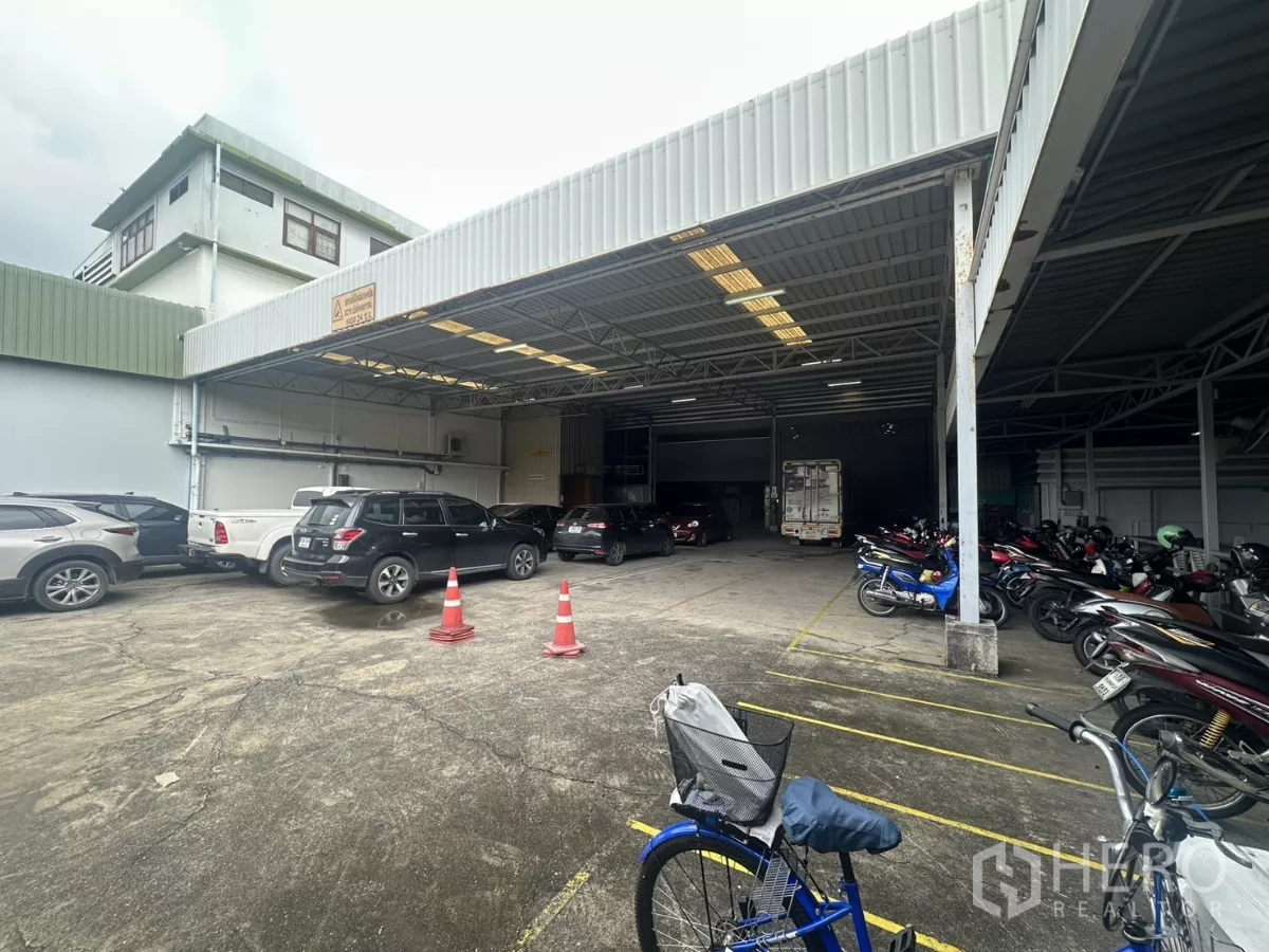 Warehouse for rent in Yan Nawa, Bangkok - Covered loading area with cars and rows of parked motorbikes beside the warehouse.