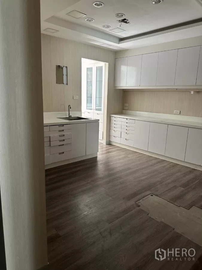 Shophouse for sale in Watthana, Bangkok - Spacious workroom with white cabinetry, recessed lights and wood-look floor.