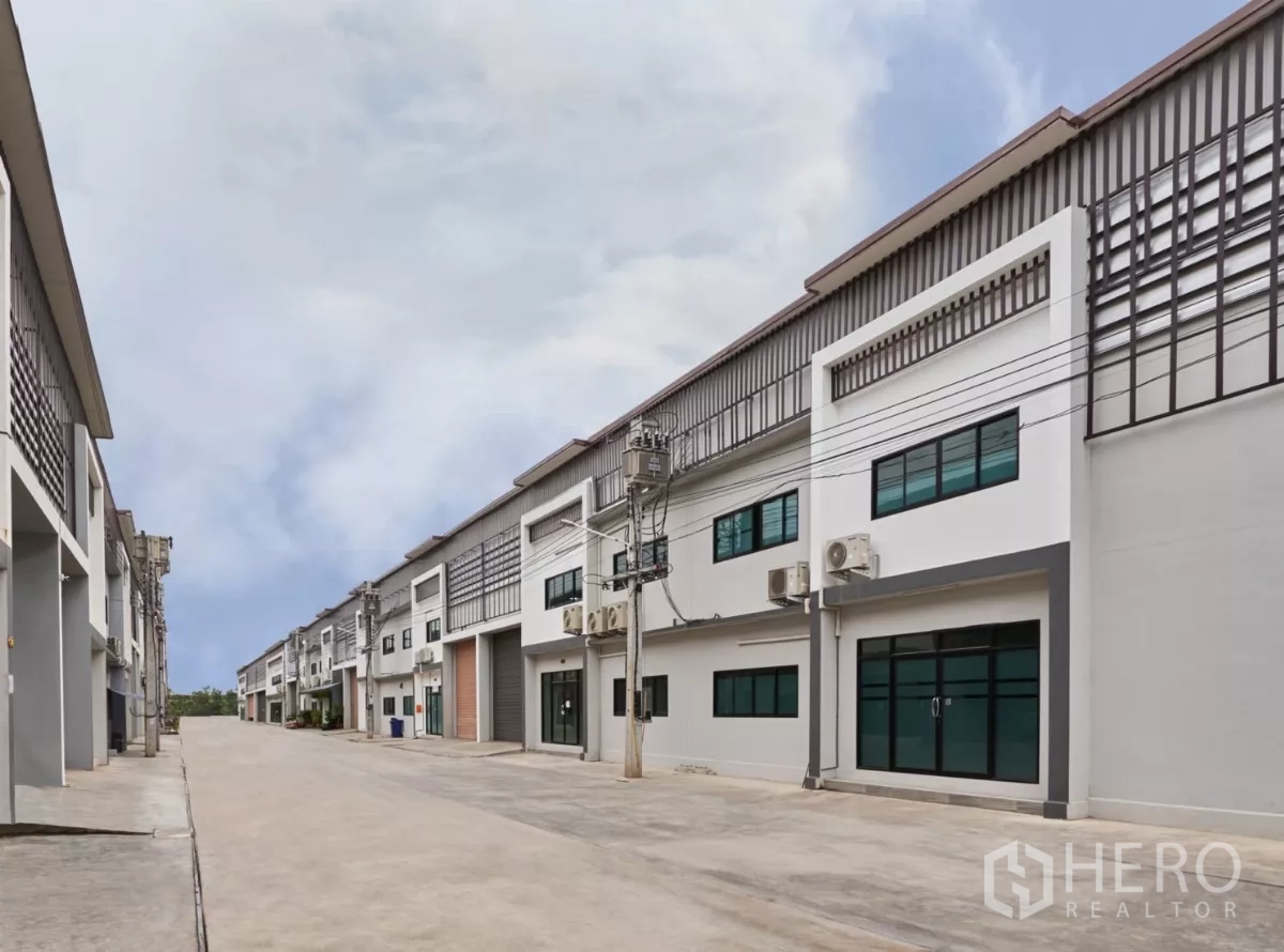 Factory for rent in Mueang Samut Sakhon, Samut Sakhon - Wide internal road between two rows of factory buildings with power poles and lines.