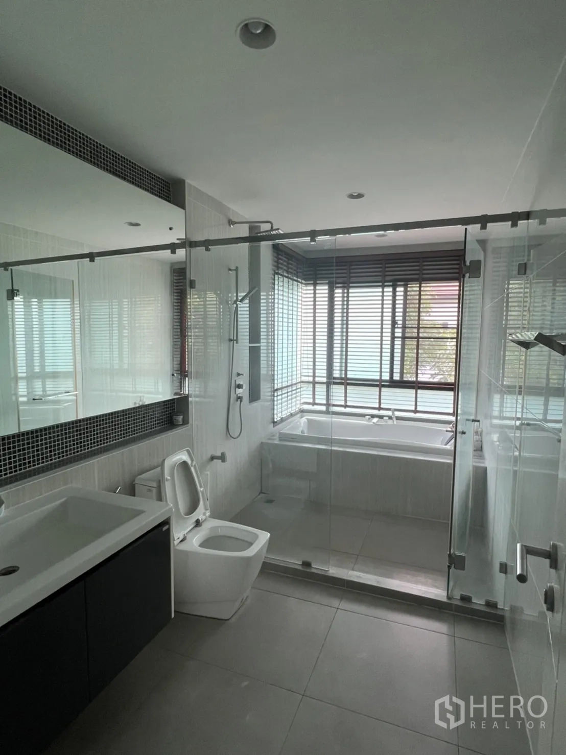 Detached House for rent or sale in Bang Kapi, Bangkok - Contemporary bathroom featuring bathtub, glass-enclosed shower, large mirror and vanity.