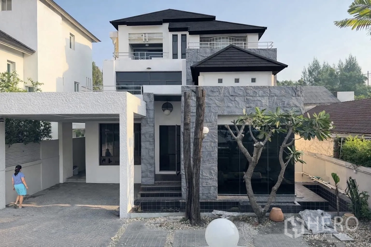 Detached House for rent in Suan Luang, Bangkok - Front elevation showing stone-clad facade, driveway and a mature frangipani tree.