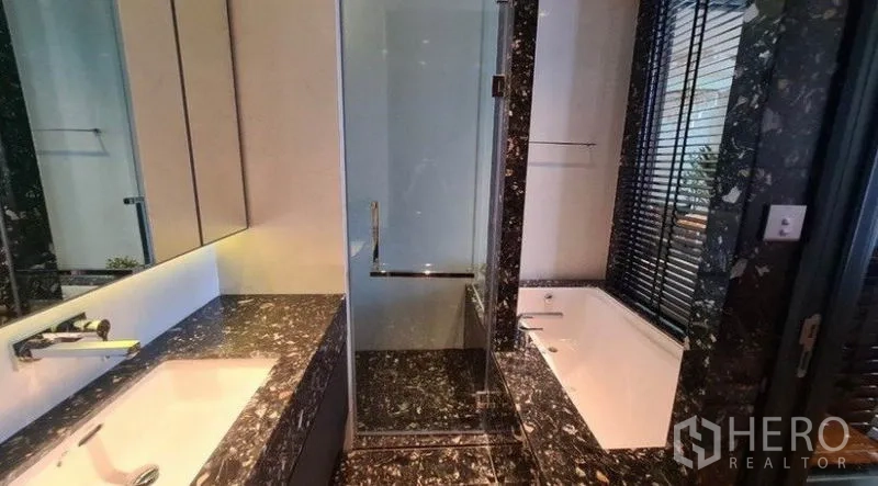 Condominium for rent in Khlong Toei, Bangkok - Modern bathroom with black marble vanity, glass shower and separate soaking bathtub by a window.