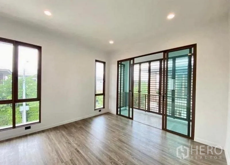 Detached House for sale in Bang Kapi, Bangkok - Upstairs room with wood flooring and glass doors to a shaded balcony with louver screens.