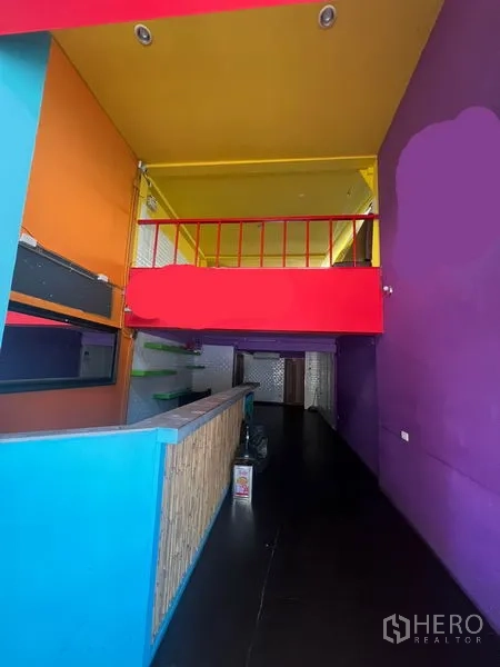 Shophouse for rent in Khlong Toei, Bangkok - Open‑plan space facing a red‑railed mezzanine and service counter, with vibrant painted walls.