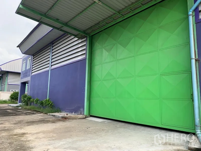 Warehouse for rent in Lam Luk Ka, Pathum Thani - Large green sliding loading door with canopy and a wide concrete yard beside the warehouse facade.