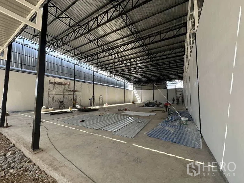 Warehouse for rent in Lam Luk Ka, Pathum Thani - Side perspective of the warehouse interior showing open floor, steel roof structure and materials on the ground