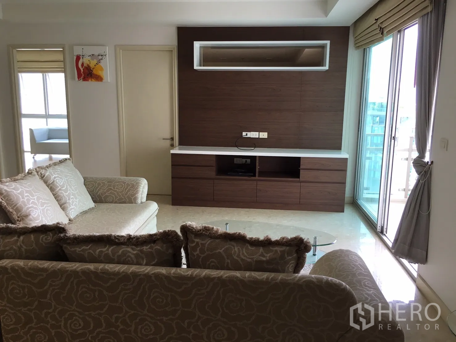Condominium for rent or sale in Khlong Toei, Bangkok - Bright living room with patterned sofa, wood media wall and sliding doors to a balcony.