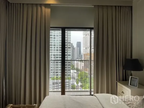 Condominium for rent in Bangkok - Bedroom with floor-to-ceiling curtains and balcony overlooking the Bangkok skyline.