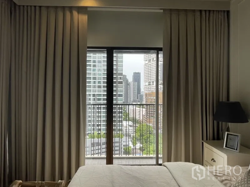 Condominium for rent in Bangkok - Bedroom with floor-to-ceiling curtains and balcony overlooking the Bangkok skyline.
