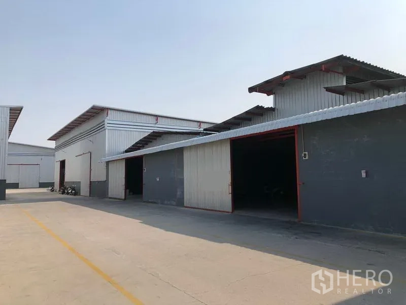 Factory for rent in Phra Pradaeng, Samut Prakan - Row of warehouse units with wide openings and paved access road for trucks.
