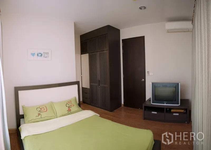 Condominium for rent in Khlong Toei, Bangkok - Third bedroom with green bedding, built-in wardrobe, TV stand and wooden flooring.