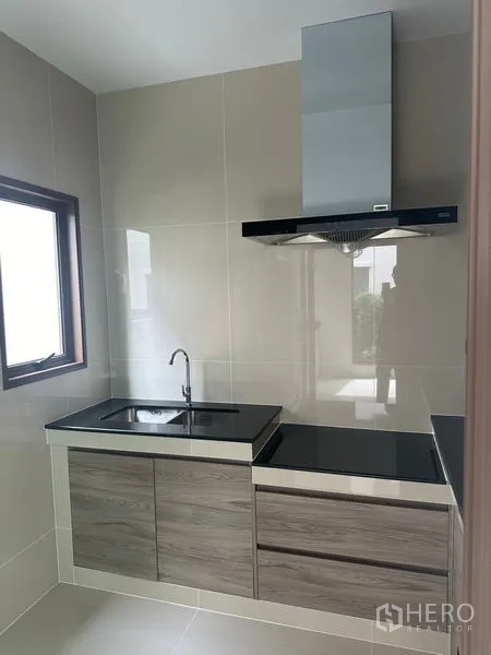 Detached House for rent in Bang Kapi, Bangkok - Closed Thai kitchen with range hood, sink and black countertops.